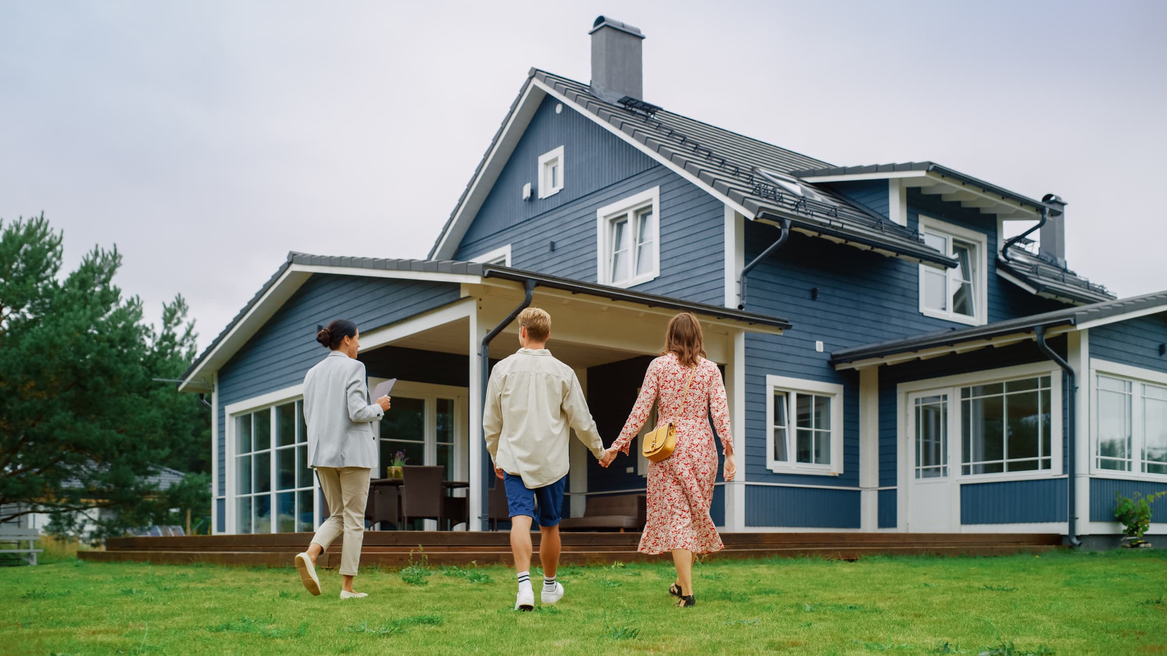 Two people holding hands next to a third person, all walking towards a house