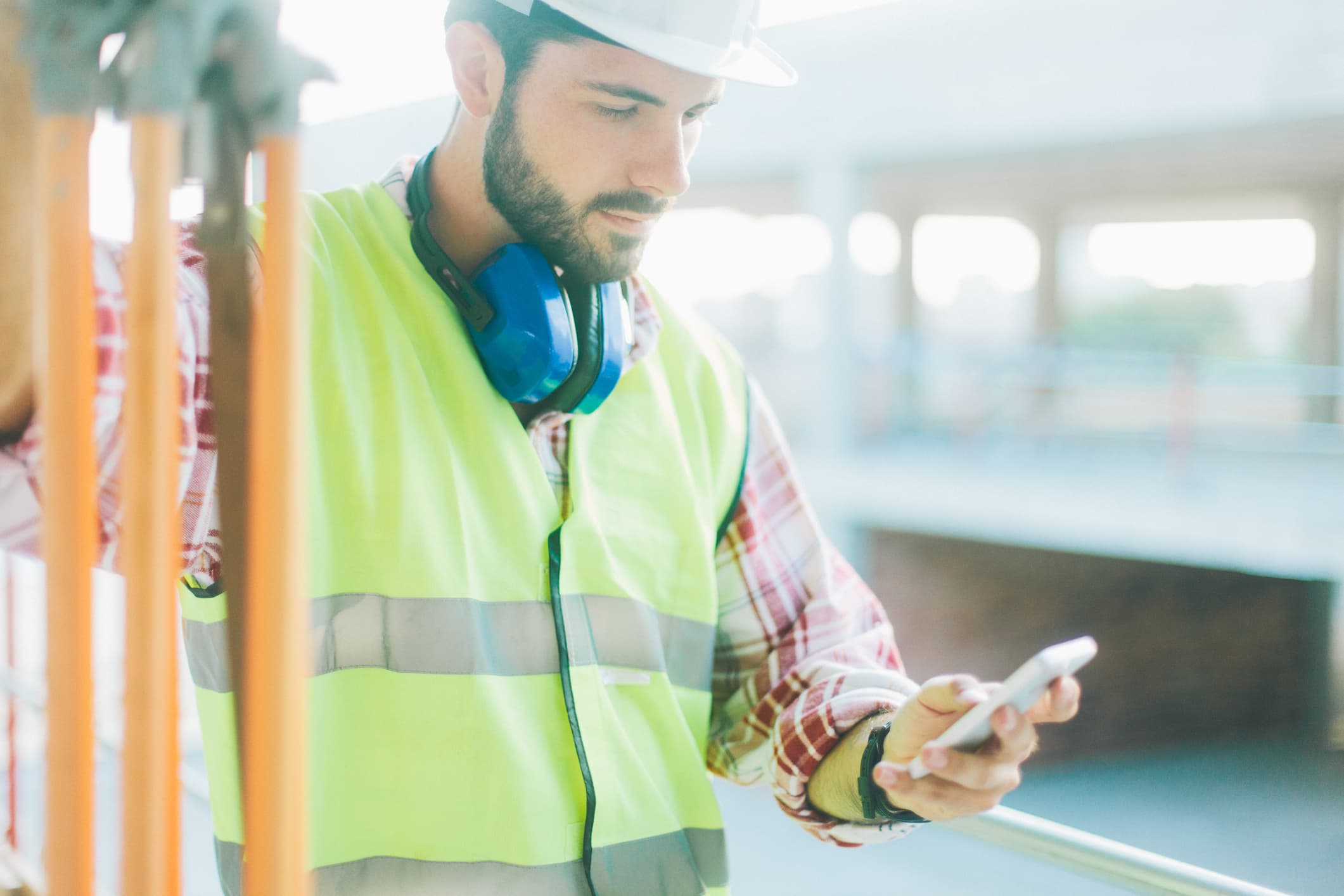 A construction worker in a reflective vest references his phone
