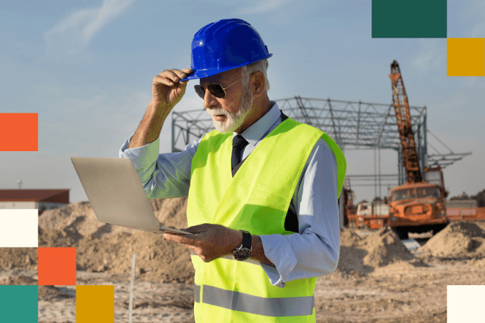 older man wearing a hard hat and reflective vest looking at tablet computer with construction crane in the background