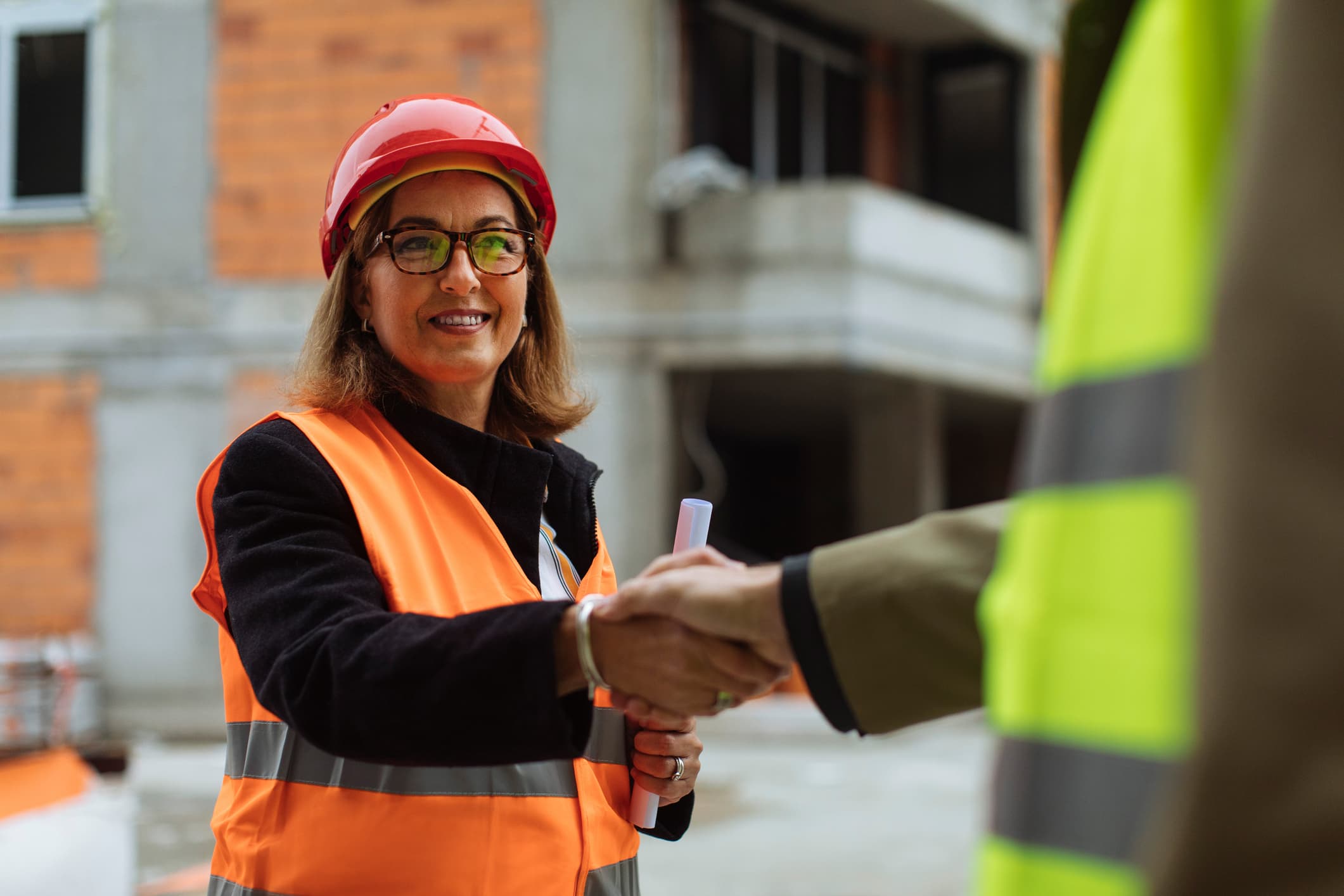 Female construction supervisor shaking hands with an unrecognizable man