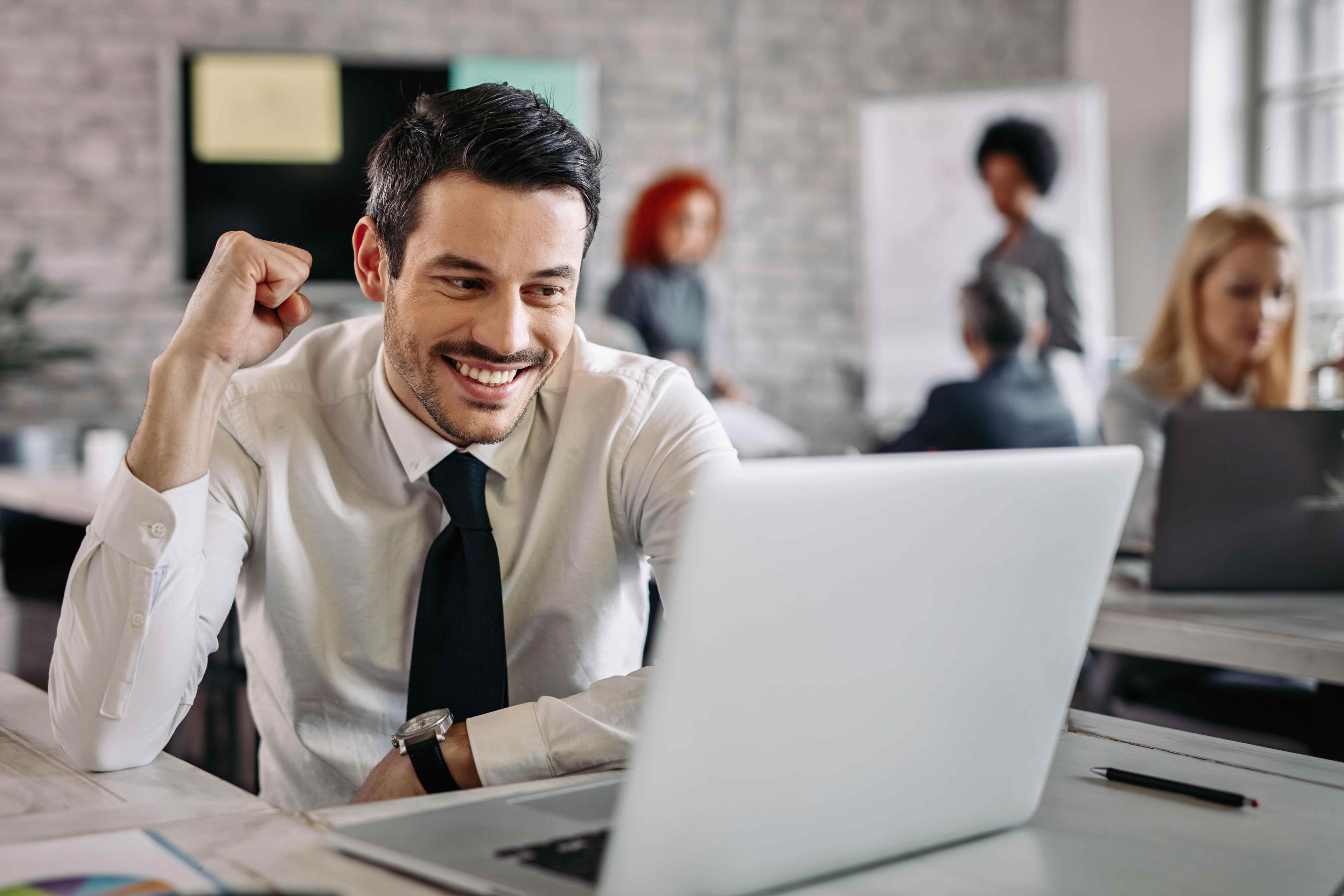 Young happy businessman using computer office celebrating good news there are people background min