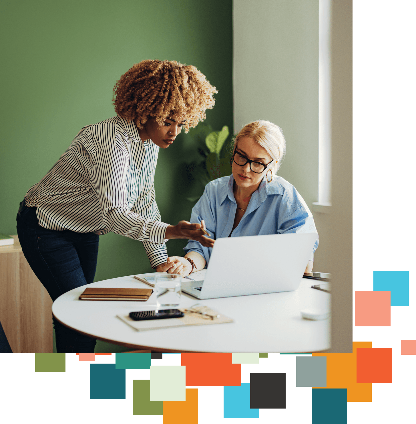Two women talk together as one references a laptop