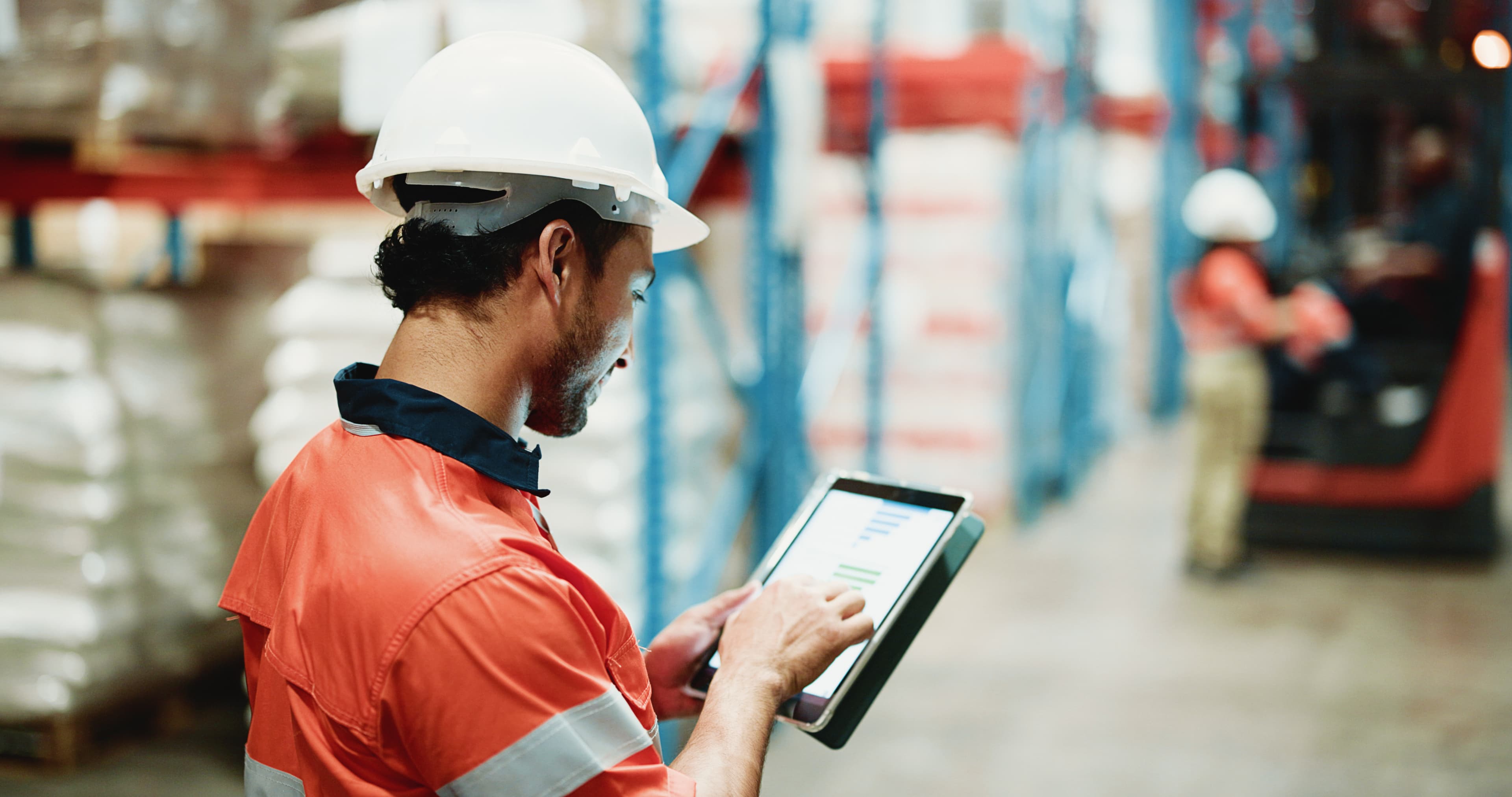 Warehouse worker in hard hat using cloud inventory management system on tablet in industrial facility.