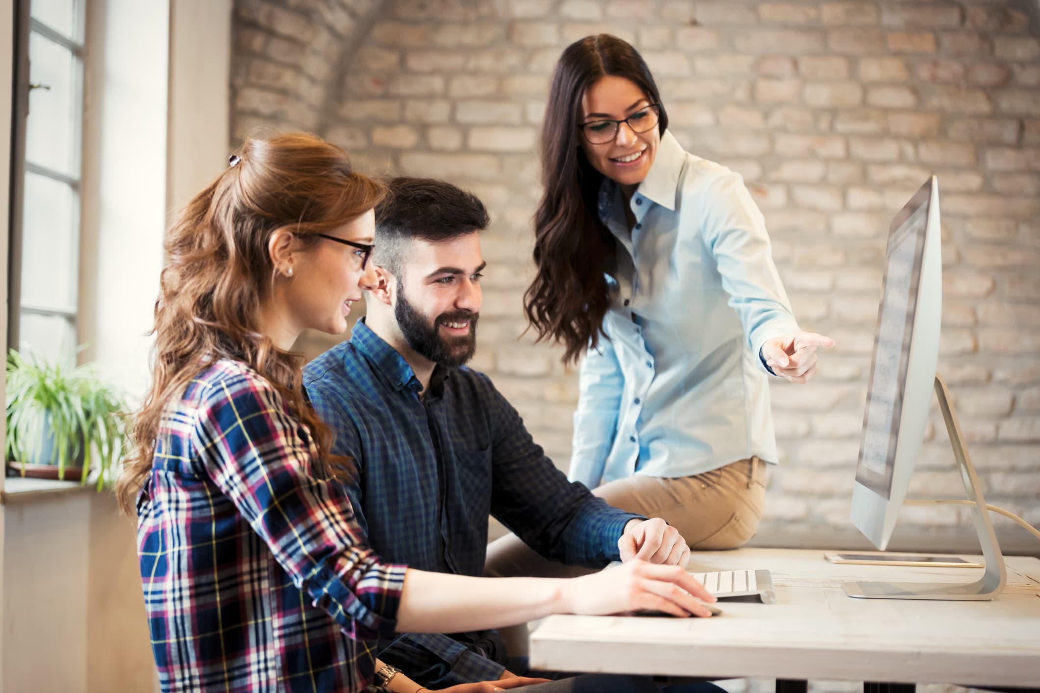 Three people discuss a project, displayed on a desktop computer