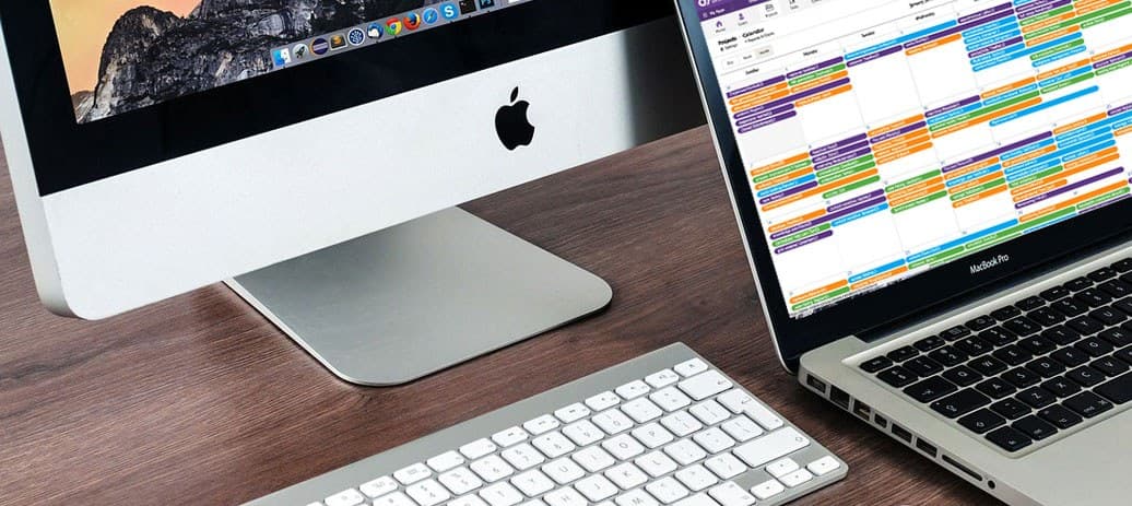 A laptop, monitor, and wireless keyboard sit together on a desk