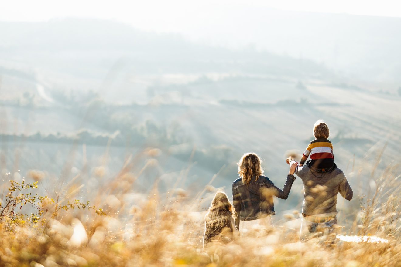 A family stands in a field and looks toward a mountain range